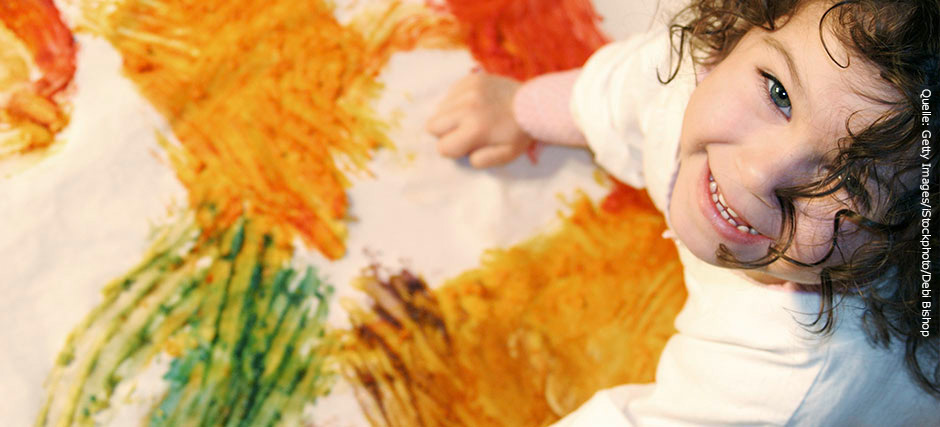 Fünfjähriges Mädchen hat bunte Farbklekse auf eine Papierplane gemalt.