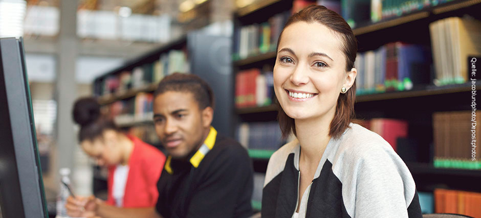 Student und Studentinnen verschiedener Hautfarben sitzen in einer Bibliothek vor Computern.