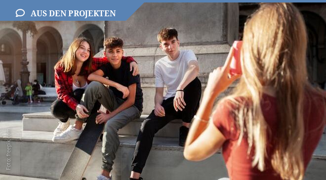 Jugendliche sitzen auf der Treppe, im Vordergrund sihet man ein Mädchen, was ein Foto von ihnen macht