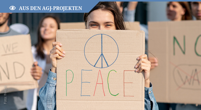 Mädchen befindet sich auf einer Demo für den Frieden und hält eine Pappe mit Peacezeichen vor sich